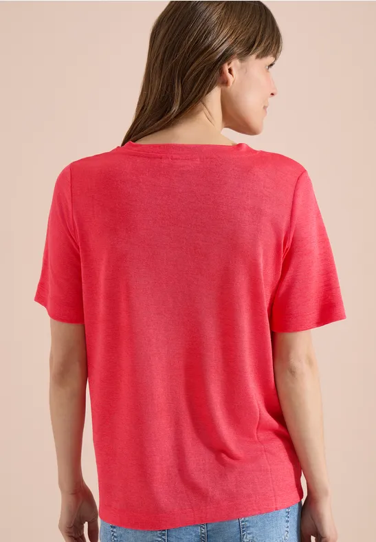 Rückansicht einer Frau mit rotem T-Shirt vor neutralem Hintergrund.