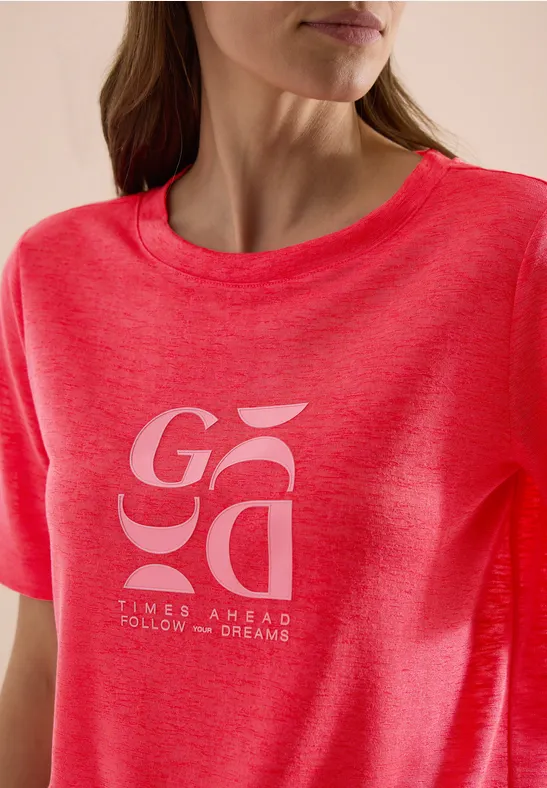 Nahaufnahme einer Frau im pinkroten T-Shirt mit Schriftzug 'GOA' und Slogan 'times ahead follow our dreams'.