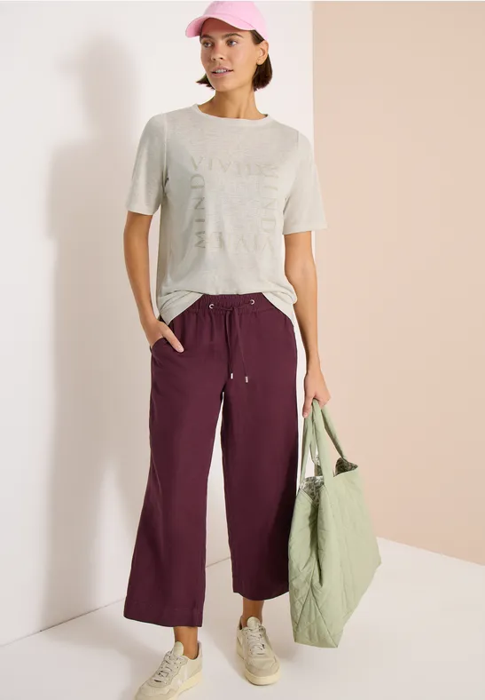 Casual look: licht t-shirt, paarse wijde broek, witte sneakers, groene tas en roze pet.