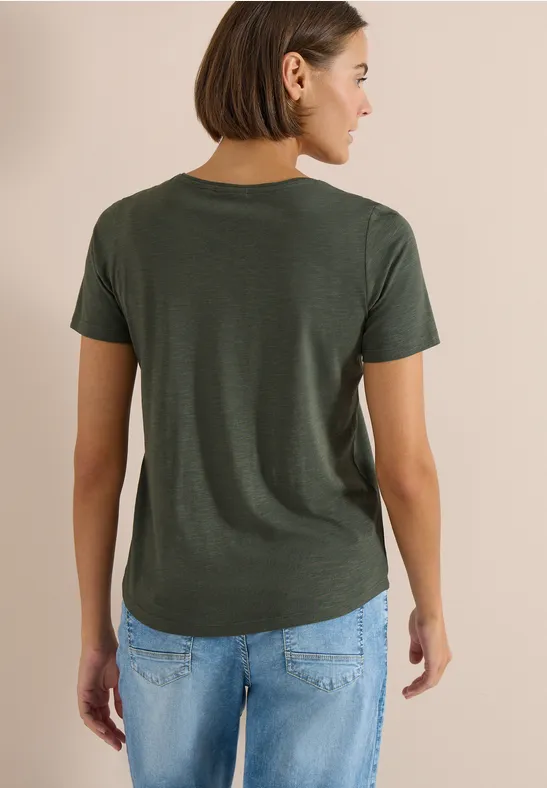 Vrouw van achteren in een donkergroen T-shirt en blauwe jeans, halflang kastanjebruin haar.