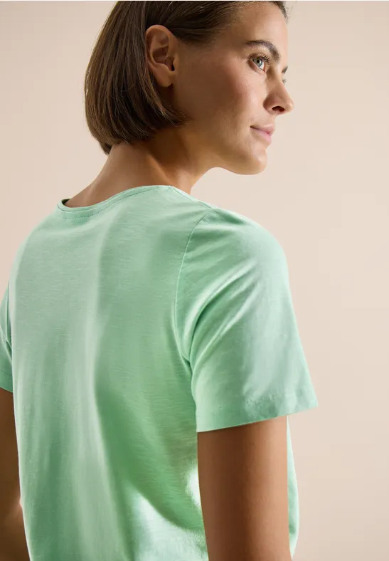 Persoon met kort haar in lichtgroen T-shirt, gezien van achteren, gezicht wazig