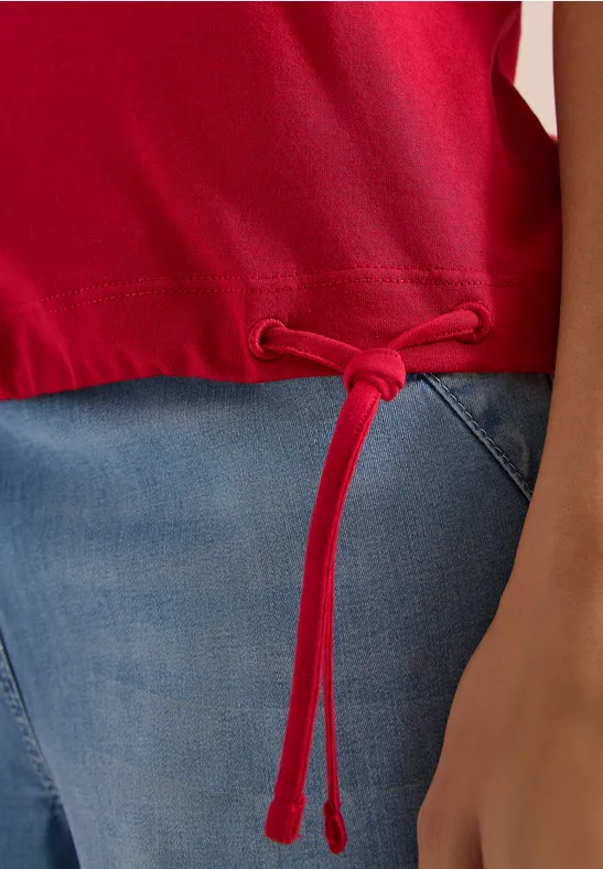 Rotes Oberteil mit Kordelzug am Saum, kombiniert mit Jeans und sichtbarem Arm.