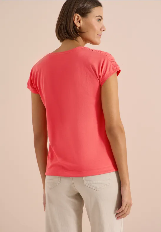 Frau von hinten in korallfarbenem T-Shirt und beigefarbenen Hosen.