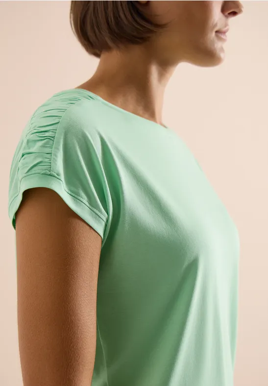 Vrouw in mintgroen T-shirt met geplooide mouwen, opzij gefotografeerd.