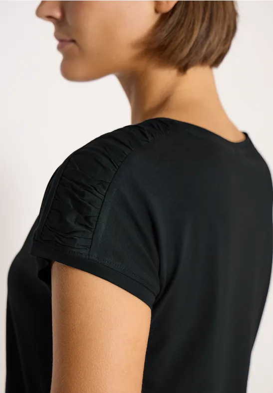 Vrouw in zijaanzicht met zwart t-shirt en geplooide mouw voor witte achtergrond