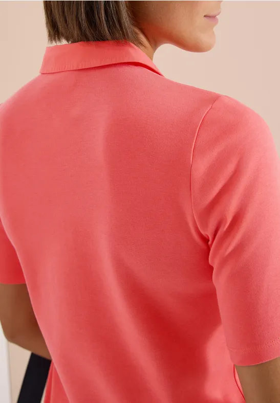 Rückansicht einer Frau, die ein korallenfarbenes Poloshirt trägt.