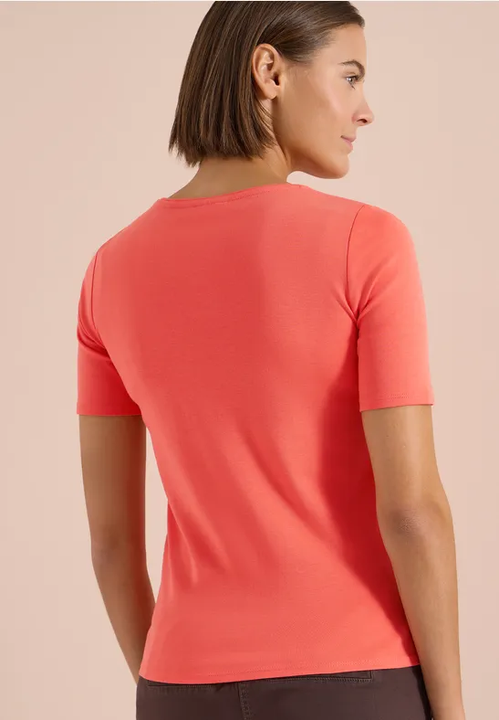 Rückenansicht einer Frau in enganliegendem, korallrotem Kurzarmshirt vor neutralem Hintergrund.