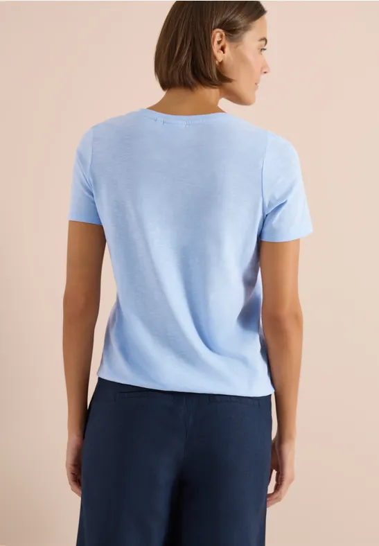 Rückansicht einer Person in hellblauem T-Shirt und dunkelblauer Hose vor beigem Hintergrund.