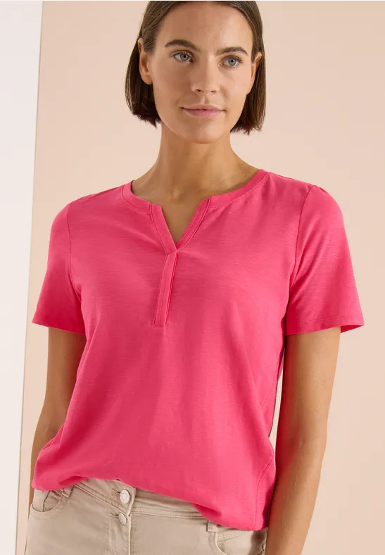 Vrouw in een roze T-shirt met korte mouwen tegen neutrale achtergrond.