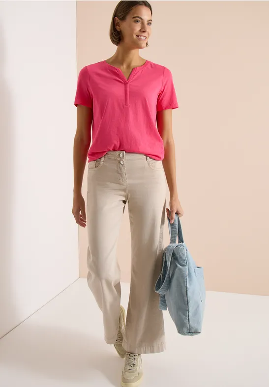 Vrouw in roze T-shirt en beige broek met lichtblauwe tas voor een neutrale achtergrond