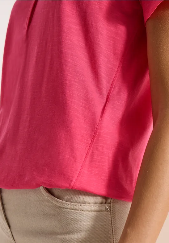 Close-up van een persoon met een felroze top en een beige broek, alleen torso en arm zichtbaar.