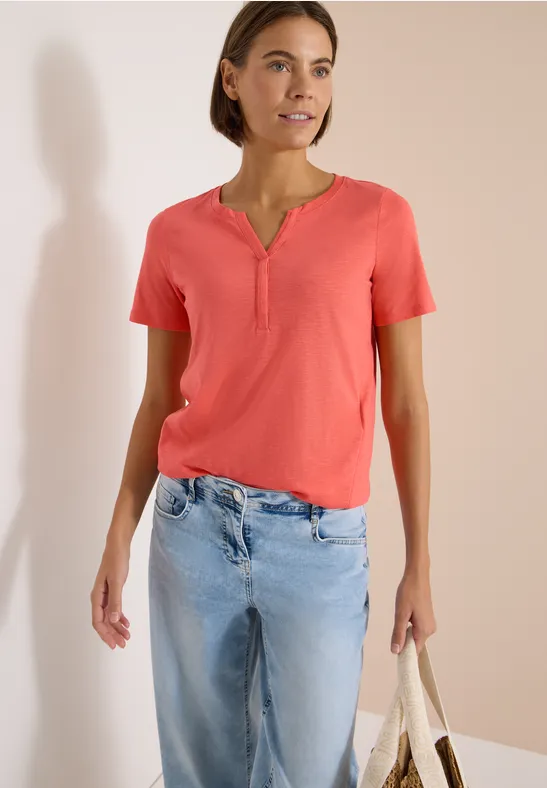Eine Frau trägt ein lachsfarbenes T-Shirt, blaue Jeans und hält eine Stofftasche.