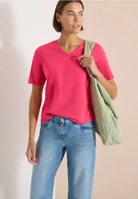 Vrouw in roze T-shirt, spijkerbroek en groene doorgestikte schoudertas voor neutrale achtergrond.