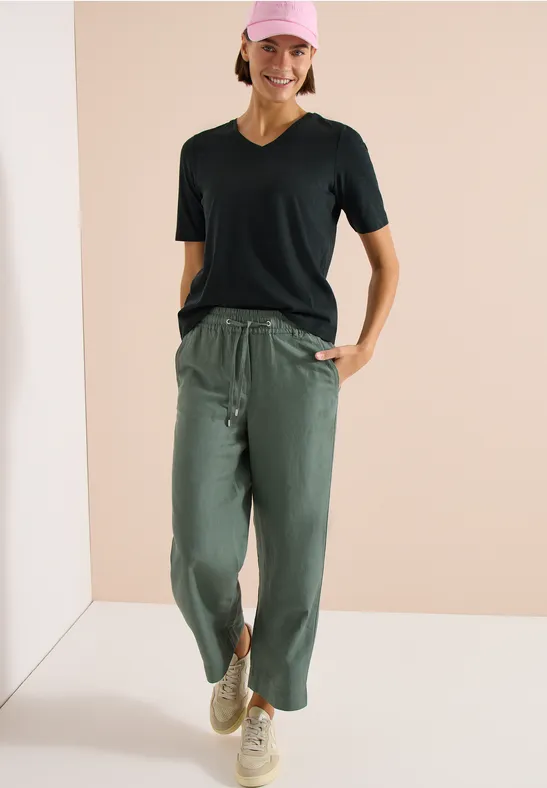 Frau in schwarzem T-Shirt, legerer olivgrüner Hose mit Tunnelzug und beigen Sneakern.