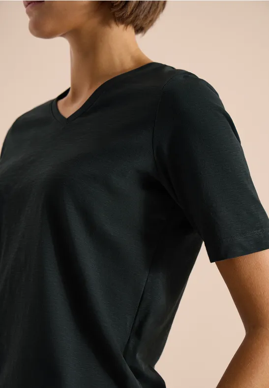 Seitliche Ansicht einer Person in schwarzem V-Shirt mit kurzen Ärmeln vor beigem Hintergrund.