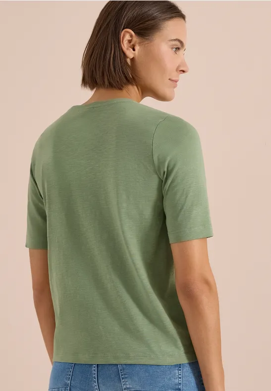 Frau von hinten in khakigrünem, kurzärmeligem T-Shirt vor neutralem Hintergrund.