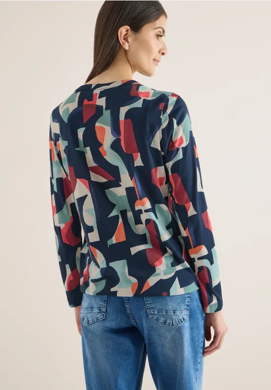 Frau von hinten in buntem, abstraktem Print-Pullover und blauen Jeans.