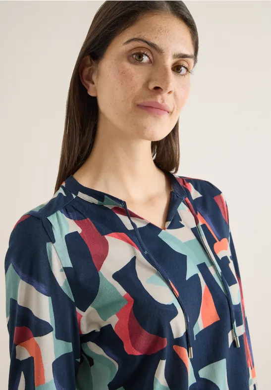 Frau in blauem Hemd mit buntem geometrischem Muster und Knopfleiste.