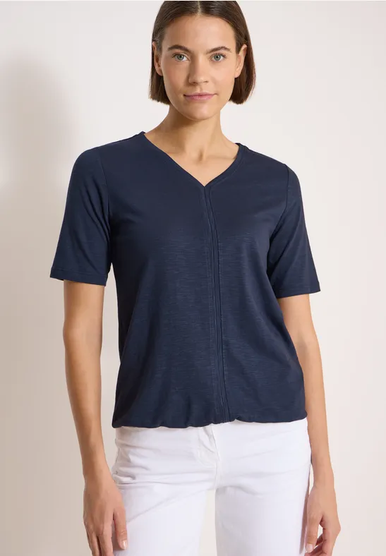 Frau trägt marineblaues V-Neck-Shirt und weiße Hose, Vorderansicht bis Hüfte.