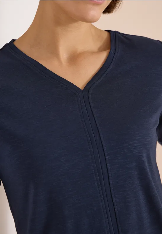 Eine Frau trägt ein dunkelblaues T-Shirt mit V-Ausschnitt und zentraler Naht.