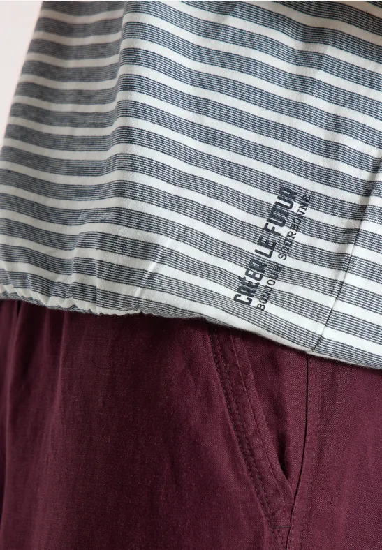 Close-up van een grijs-wit gestreept shirt met opdruk en een wijnrode broek.