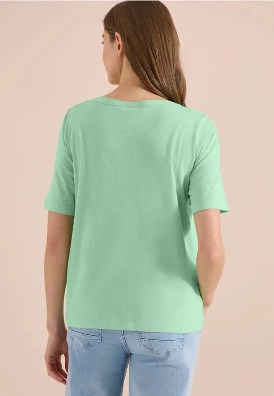 Frau steht mit dem Rücken zur Kamera, trägt ein hellgrünes T-Shirt und blaue Jeans.