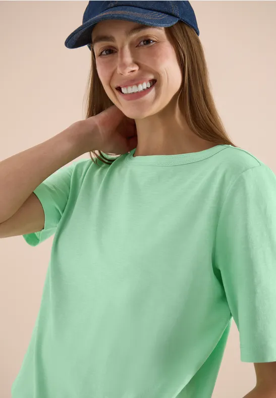 Person mit grünem T-Shirt und blauem Cap, Gesicht unkenntlich