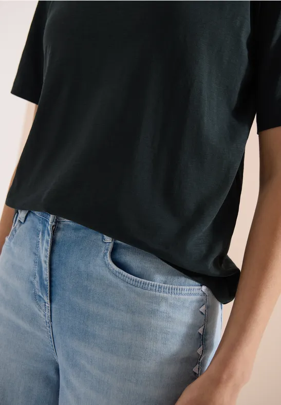 Person trägt schwarzes T-Shirt und helle Jeans, Nahaufnahme von Oberkörper und Händen.