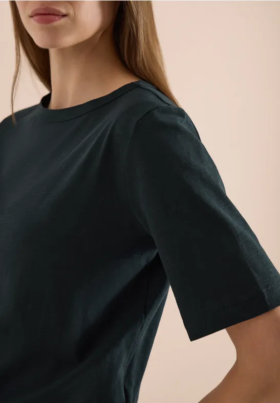 Nahaufnahme einer Frau in einem schlichten schwarzen T-Shirt mit halblangen Ärmeln.