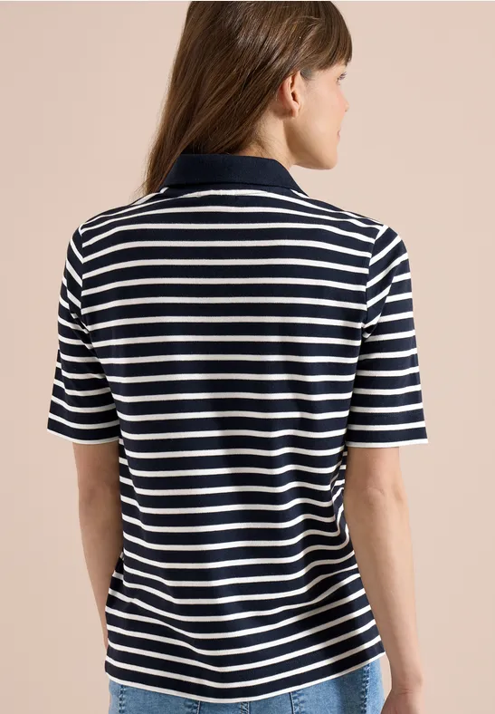 Eine Person von hinten in einem blau-weiß gestreiften kurzärmeligen Poloshirt vor beigem Hintergrund.