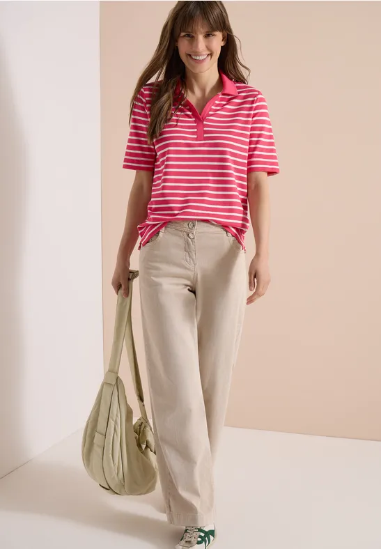 Frau trägt pink-weiß gestreiftes Polo, beige weite Hose und grüne Umhängetasche.