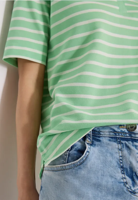 Eine Person trägt ein grünes T-Shirt mit weißen Streifen und eine helle Jeanshose.