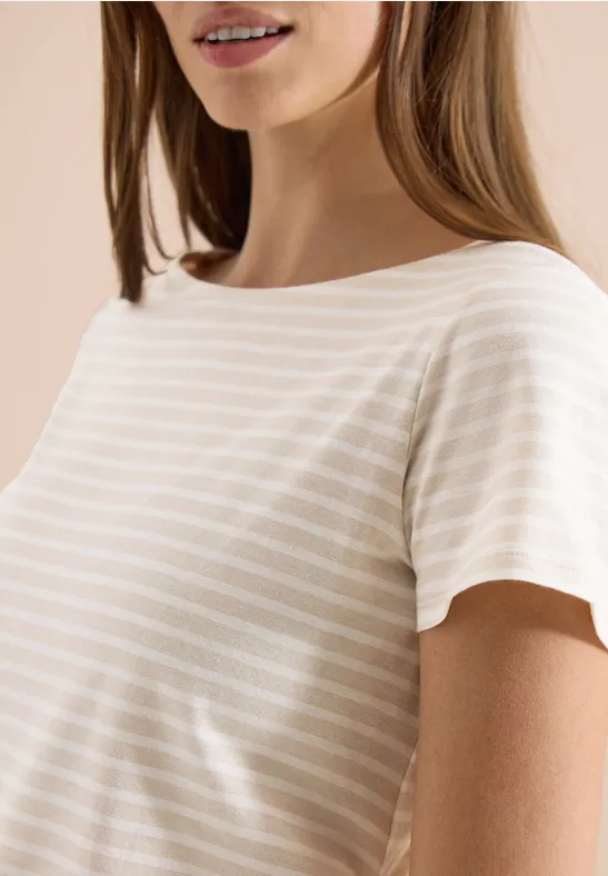 Eine Frau trägt ein beiges, gestreiftes T-Shirt vor beigem Hintergrund.