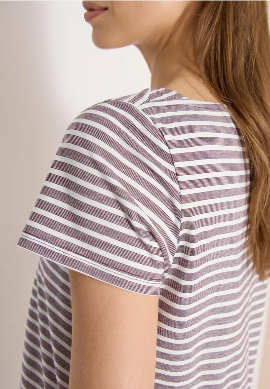 Seitliche Aufnahme einer Frau mit braunen Haaren im weiß-lila gestreiften T-Shirt vor weißem Hintergrund.