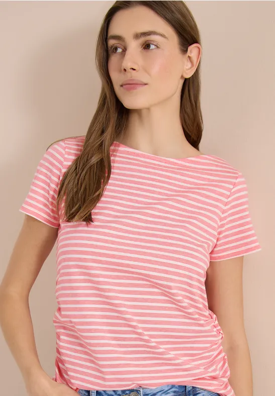 Eine junge Frau trägt ein rosa-weiß gestreiftes T-Shirt mit kurzen Ärmeln vor neutralem Hintergrund.