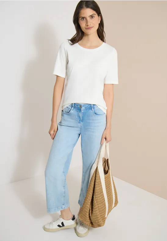 Vrouw met wit t-shirt, lichtblauwe jeans, sneakers en grote strooien tas.