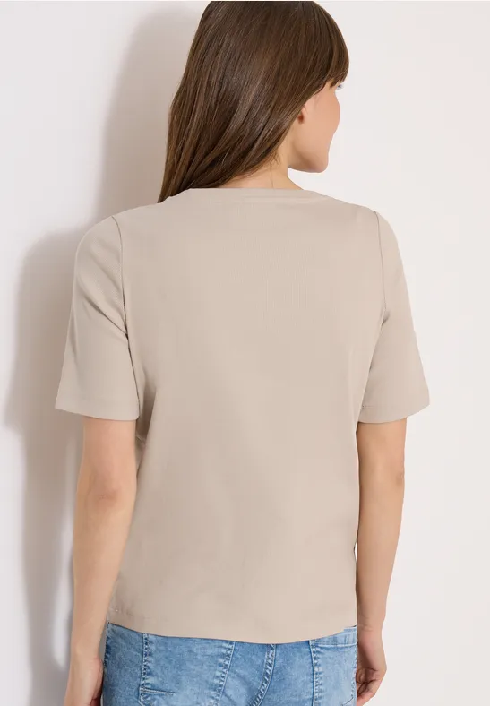 Frau von hinten in beigefarbenem T-Shirt und blauen Jeans.