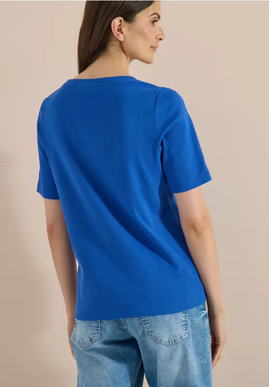 Een persoon heeft de rug naar de camera gekeerd, draagt een koningsblauw T-shirt en blauwe spijkerbroek.