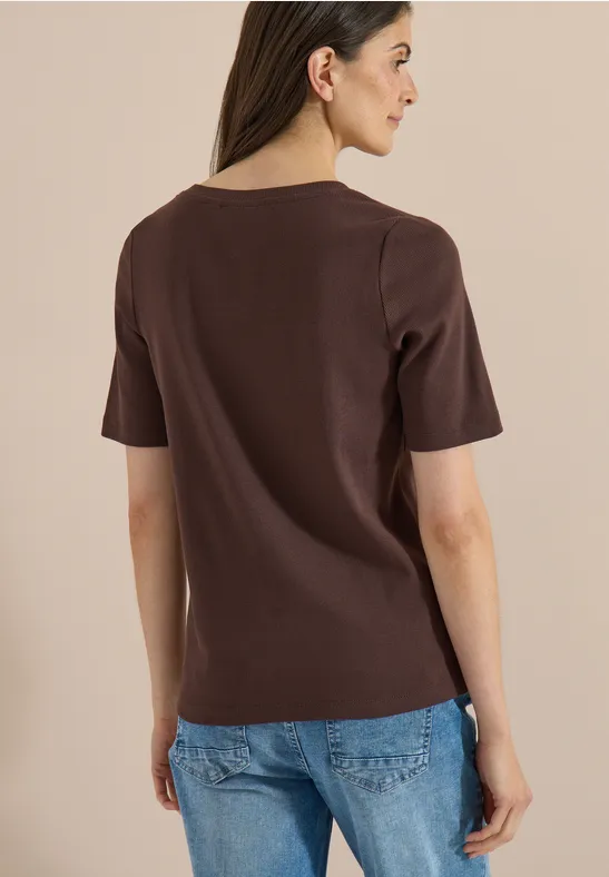 Vrouw gefotografeerd van achteren in een bruin T-shirt en blauwe spijkerbroek voor neutrale achtergrond.