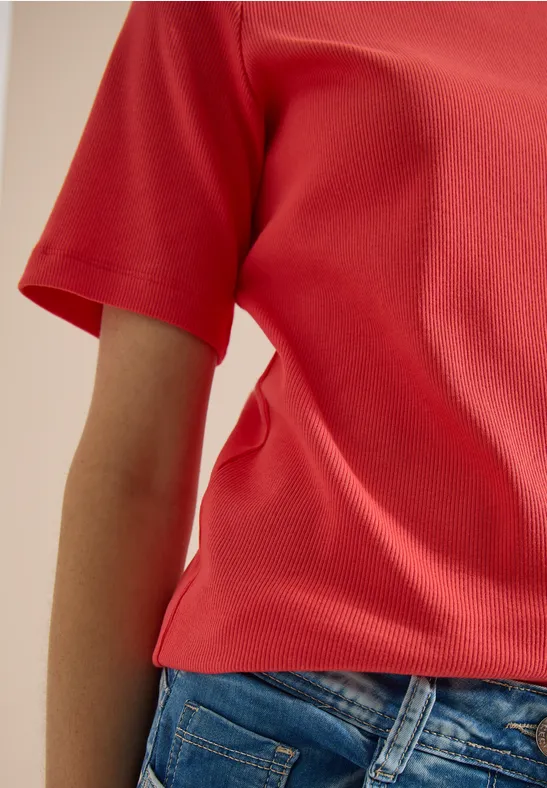 Een persoon draagt een rood shirt en blauwe jeans, gedeeltelijke weergave van het bovenlichaam