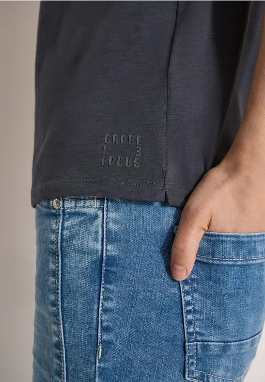 Torso mit dunkelgrauem T-Shirt und aufgedrucktem Logo, Hand in der vorderen Tasche blauer Jeans.