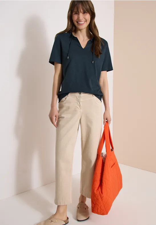 Frau trägt kurzärmliges dunkelblaues Hemd, beigefarbene Hose, beige Schuhe und orangefarbene Tasche