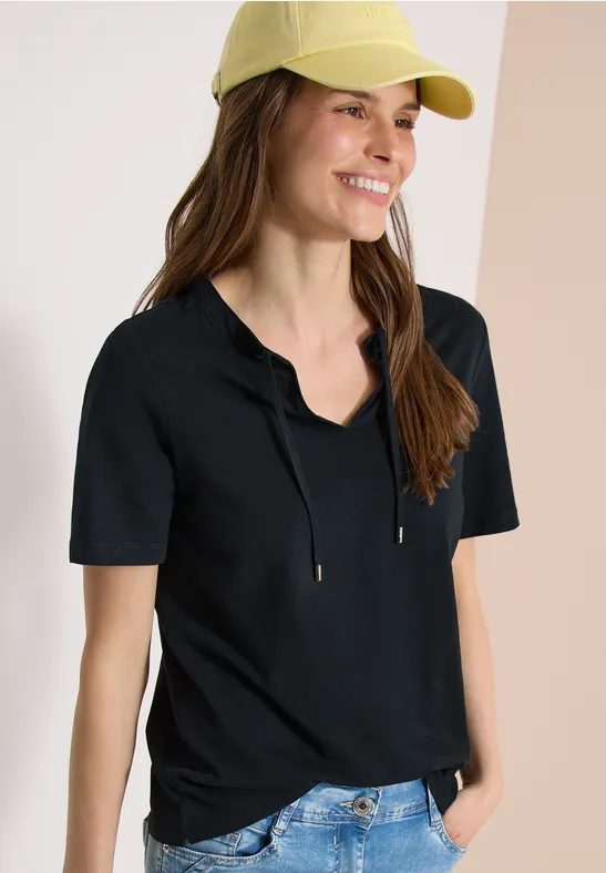 Personne en tee-shirt court à capuche noir, casquette jaune et jean bleu.