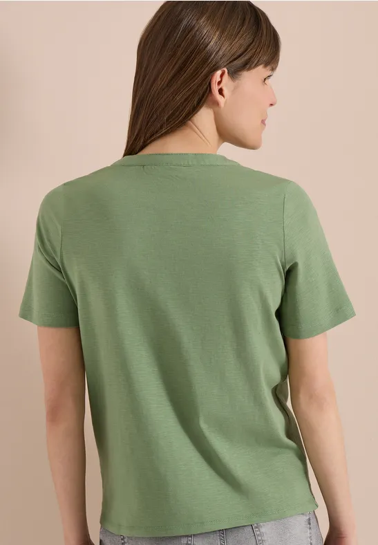Femme vue de dos portant un T-shirt vert sur un fond neutre.