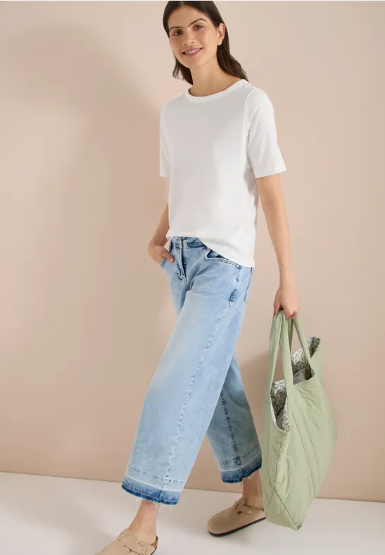 Vrouw in wit t-shirt, wijde jeans en groene gewatteerde tas voor beige achtergrond.