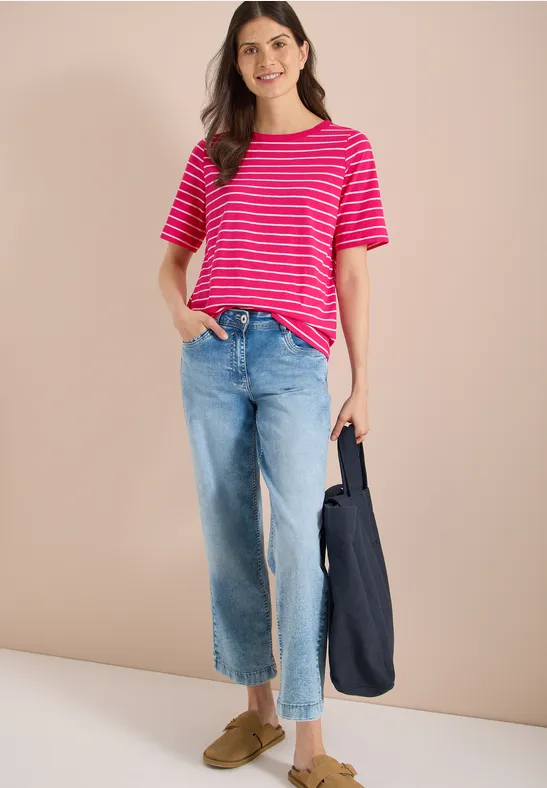 Persoon draagt rood-wit gestreept T-shirt, wijde blauwe spijkerbroek, olijfgroene loafers en een donkerblauwe tas.