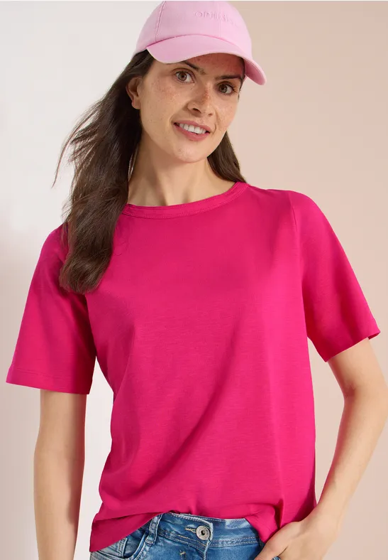 Vrouw met roze t-shirt en lichtroze pet tegen een neutrale achtergrond.
