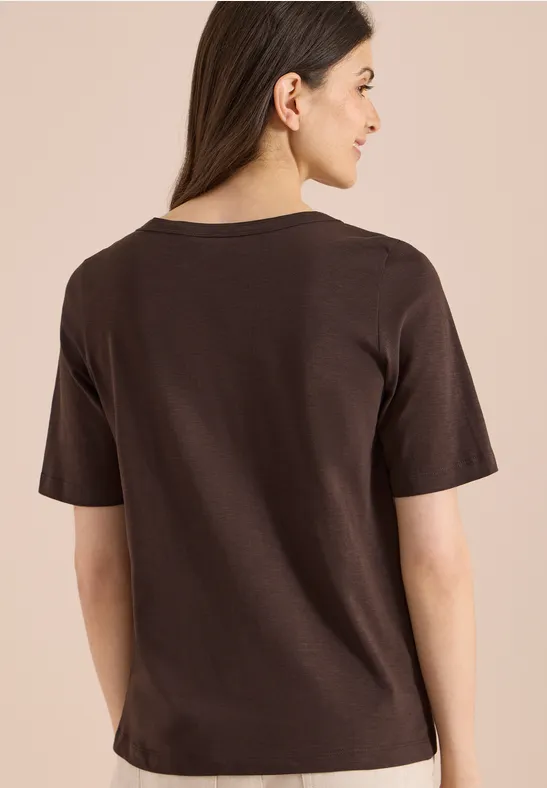 Vrouw van achteren in effen bruin T-shirt tegen een neutrale achtergrond.