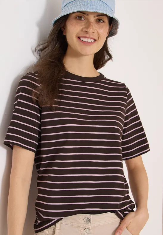 Jonge vrouw in gestreept T-shirt en hoed die de zoom van haar shirt recht trekt.