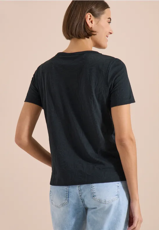 Person in schwarzem T-Shirt und hellen Jeans von hinten vor beigem Hintergrund.